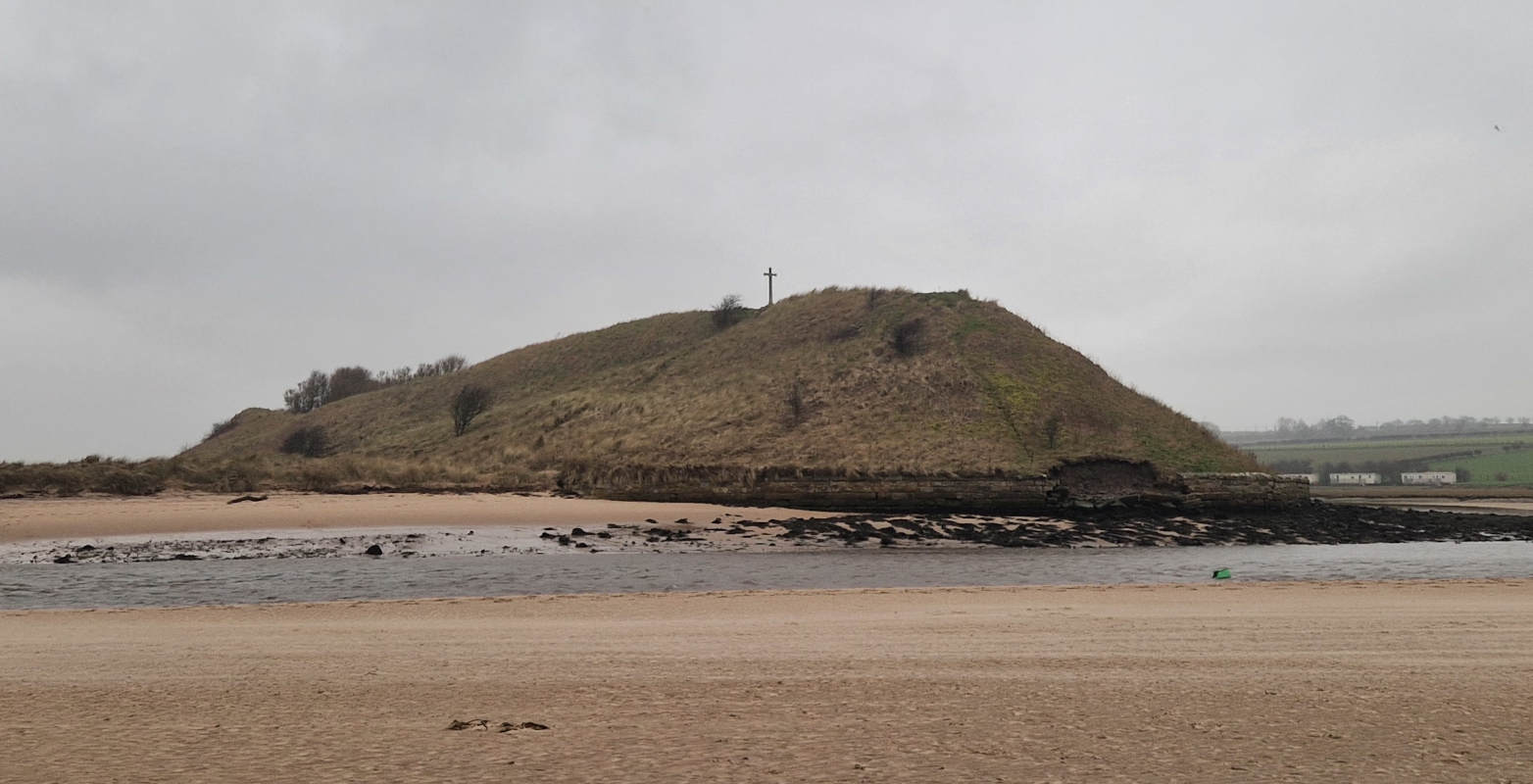 A duny hill that rises on the opposite shore of a shallow river, topped with a wooden cross