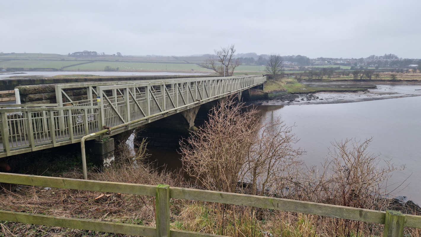 A girdered bridge passing over quiet waters