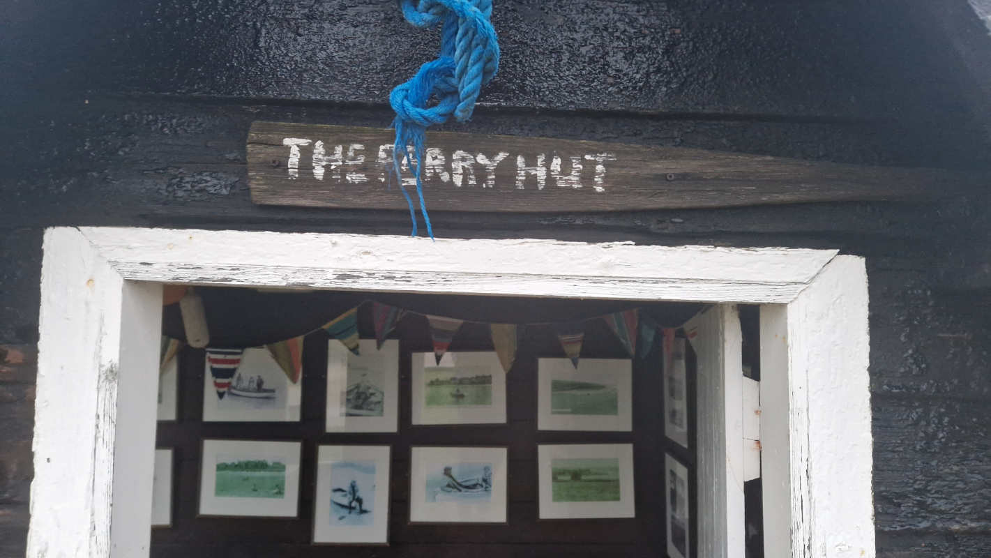 The entrance to a small hut; above the door is a painted oar reading "The Ferry Hut"