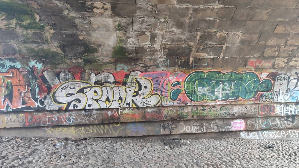 Graffiti covers the walls of an archway underpass, its floor tiled with loose cobbles